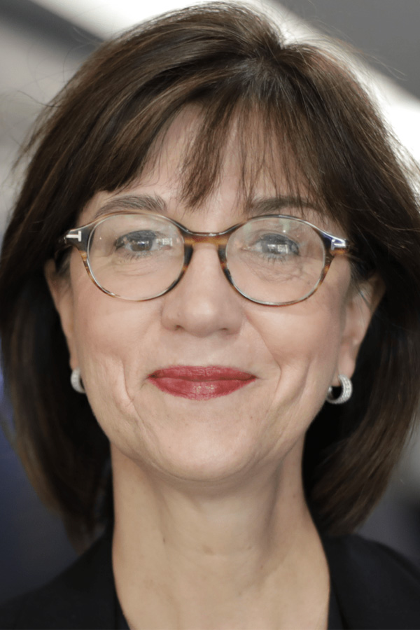 An image of a woman with shoulder length hair smiling to camera, she wears glasses